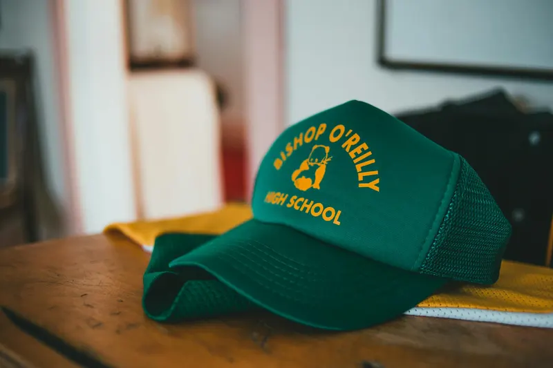 Close-up of a green Bishop O'Reilly High School cap on a wooden desk indoors.