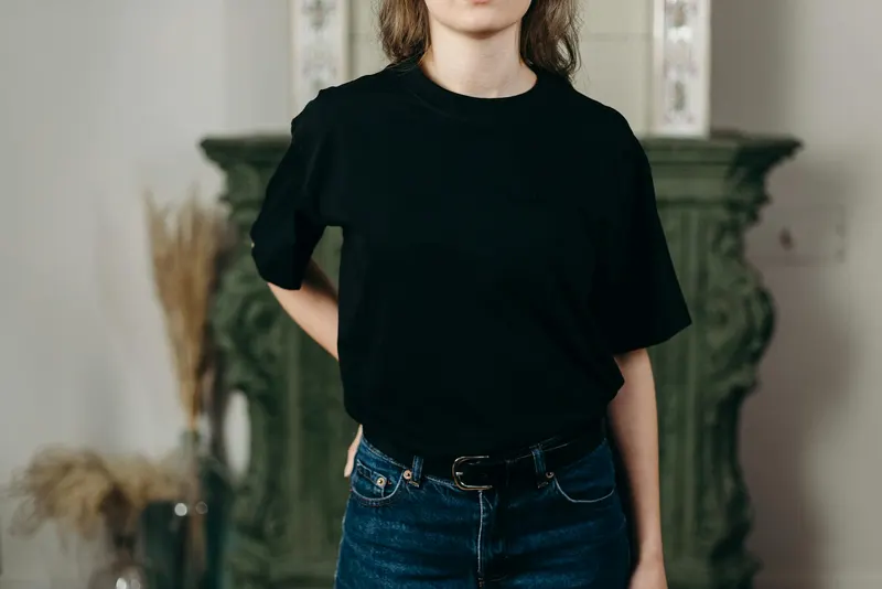 Faceless model in black t-shirt and jeans showcasing minimalist fashion style indoors.
